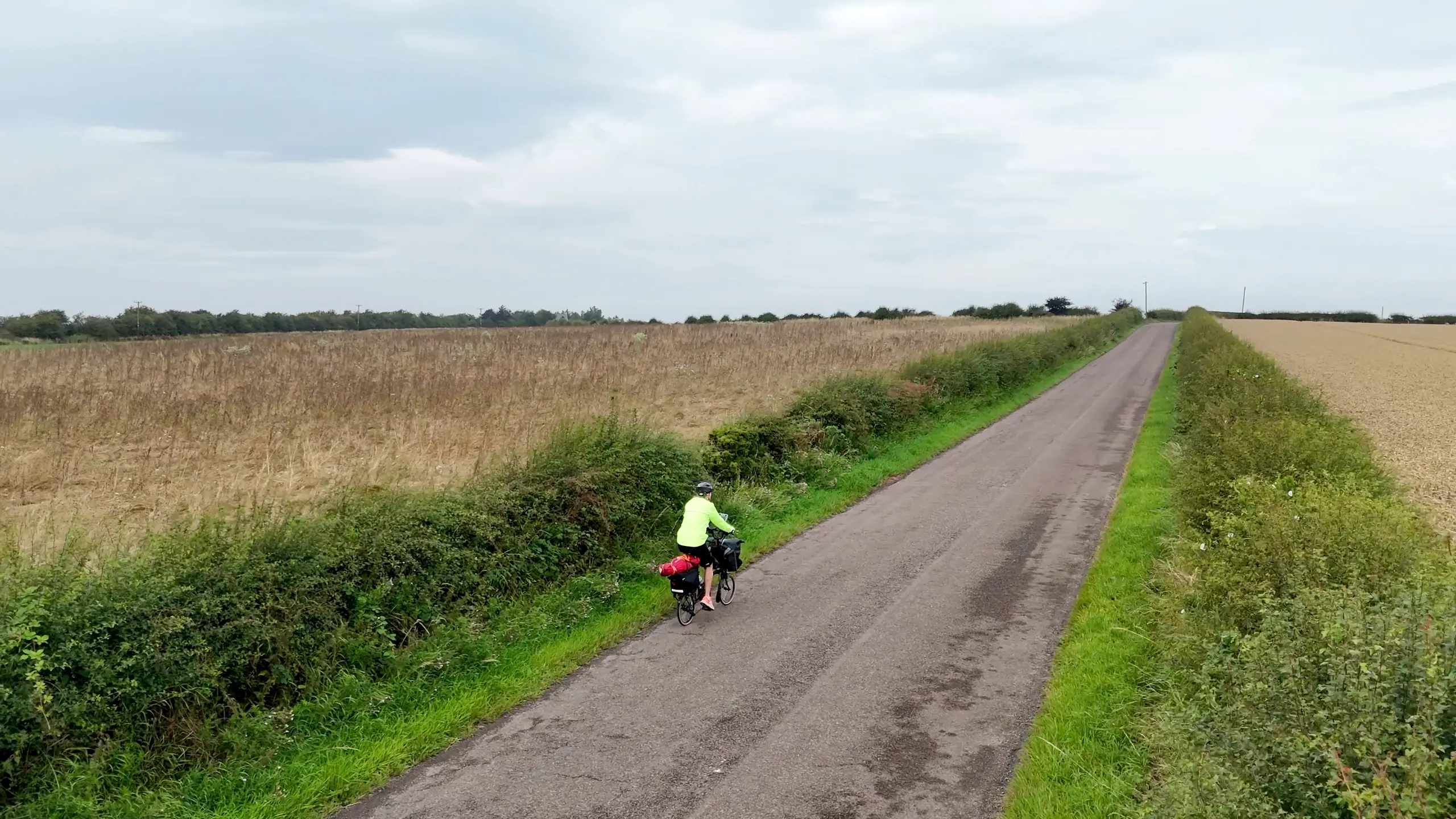 Amy riding the Brompton away down a lane between the hedges and the barley