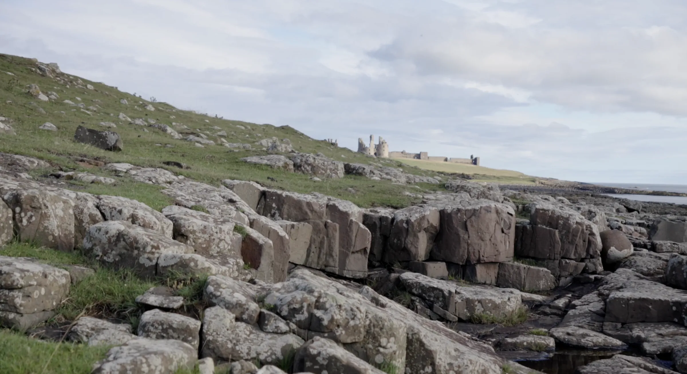 Dunstanburgh Castle on the clifftop above the rocky Northumberland shore